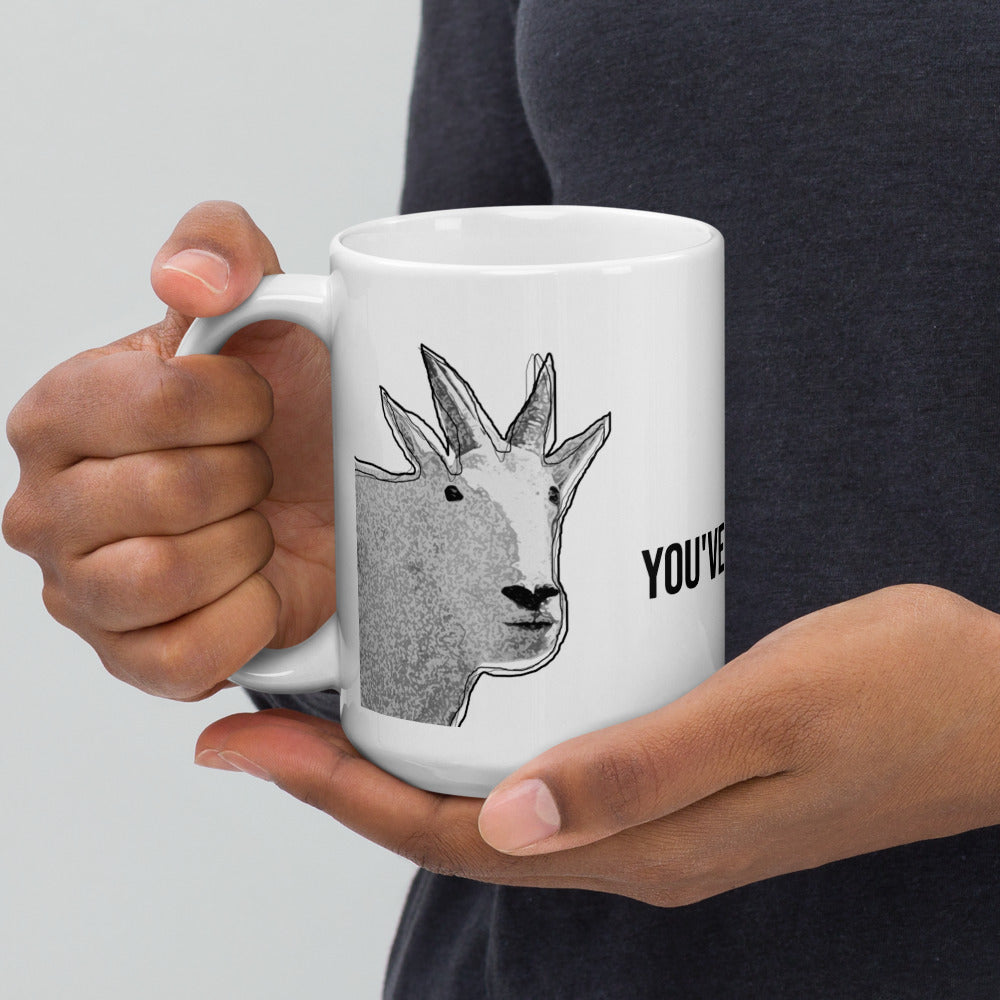 A pair of hands holding a white glossy mug that has a funny and unique mountain goat design.