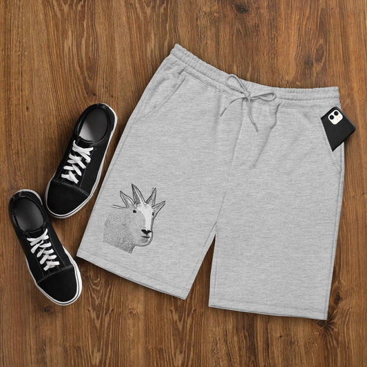 A pair of grey Men's fleece shorts designed by North American Mountain Goat Appreciation Club that features a unique funny mountain goat design, placed on a natural wooden floor beside a pair of black sneakers.