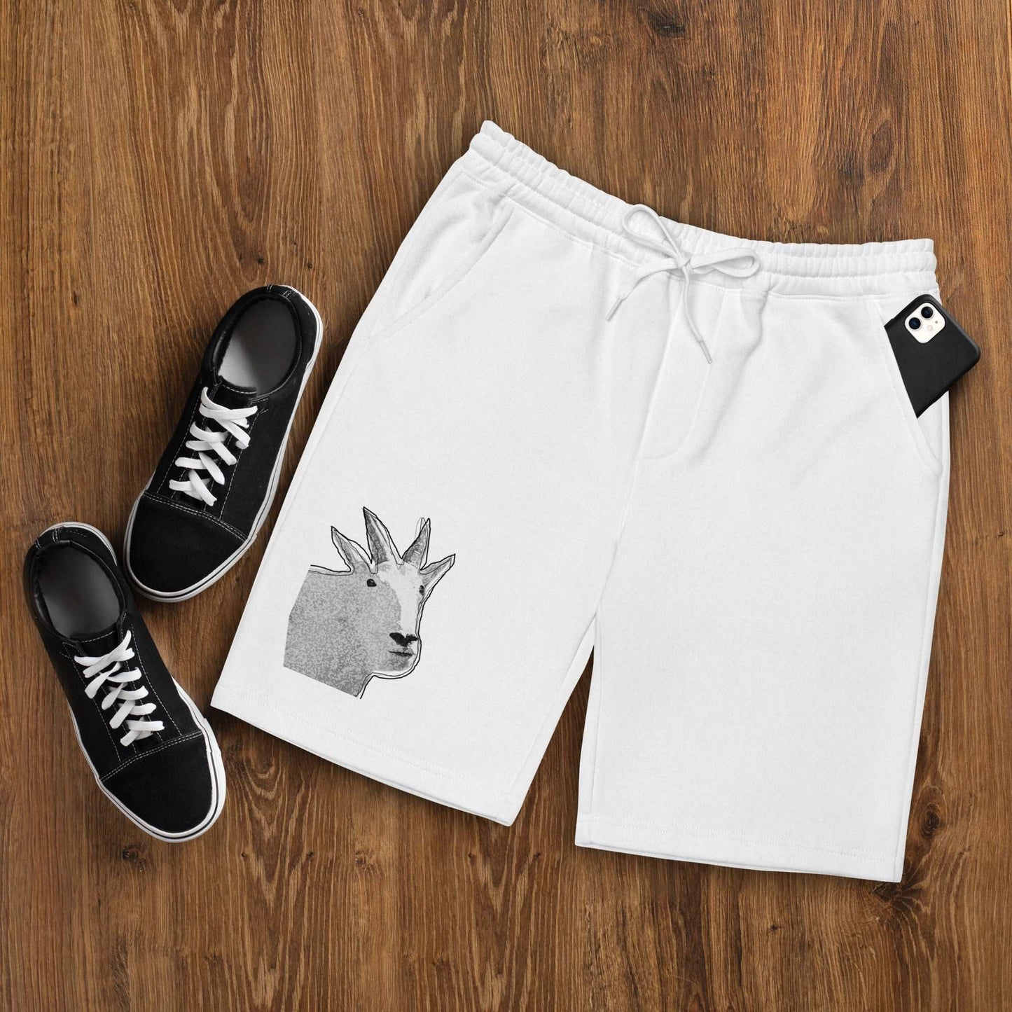 A pair of white Men's fleece shorts designed by North American Mountain Goat Appreciation Club that features a unique funny mountain goat design, placed on a natural wooden floor beside a pair of black sneakers.