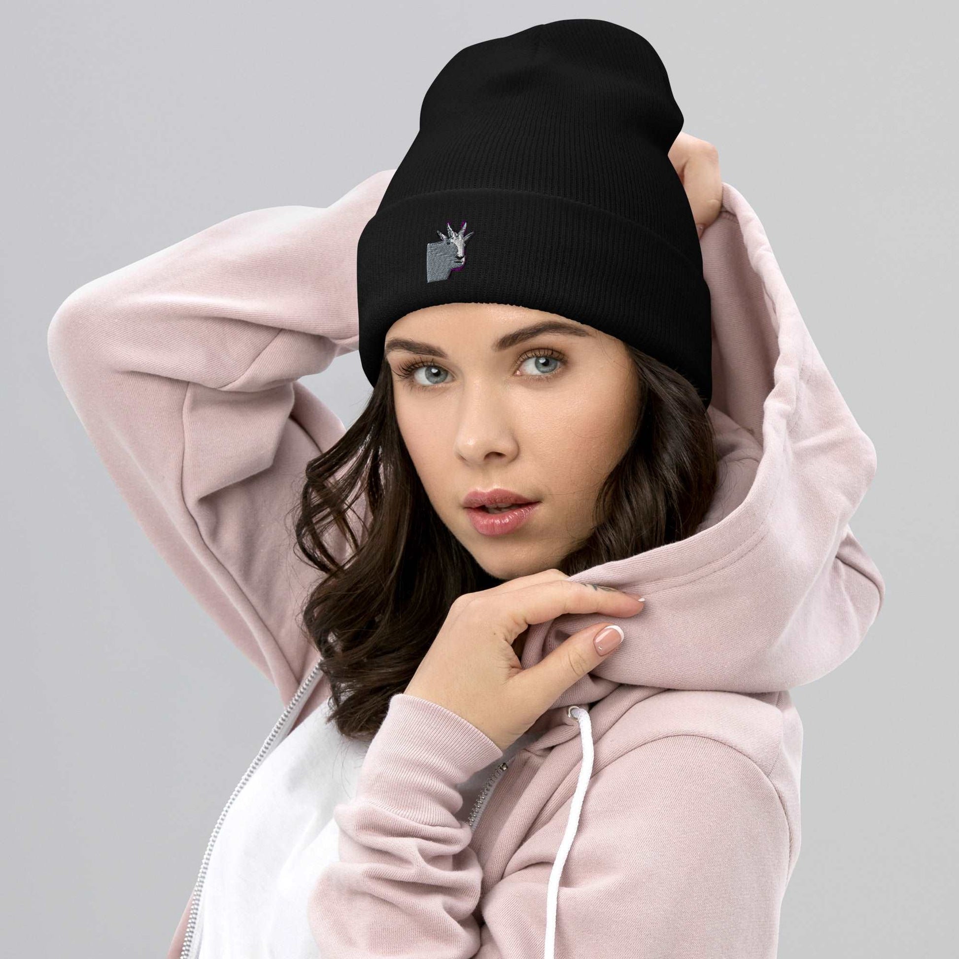 A female model wearing a high-quality black unisex cuffed beanie that has an embroidery of a funny mountain goat design.