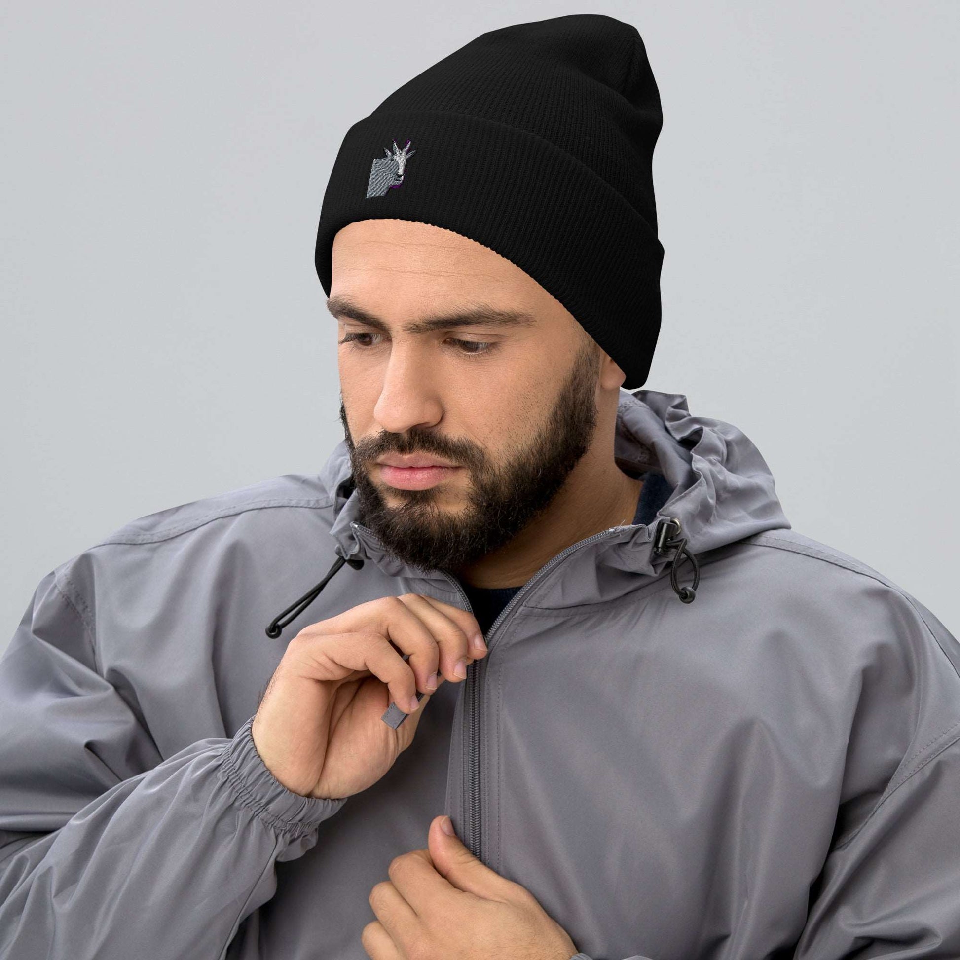 A male model wearing a high-quality black unisex cuffed beanie that has an embroidery of a funny mountain goat design and a running jacket.