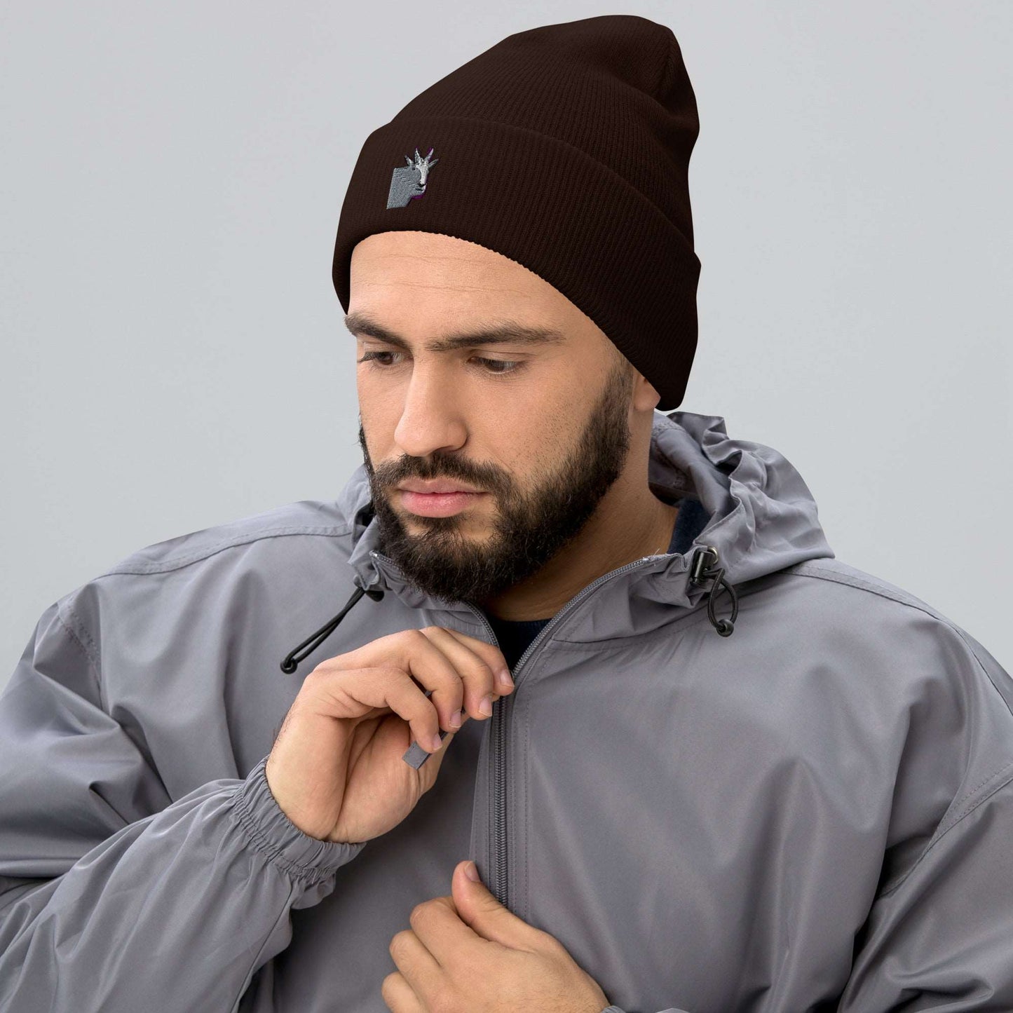 A male model wearing a high-quality brown unisex cuffed beanie that has an embroidery of a funny mountain goat design and a running jacket.