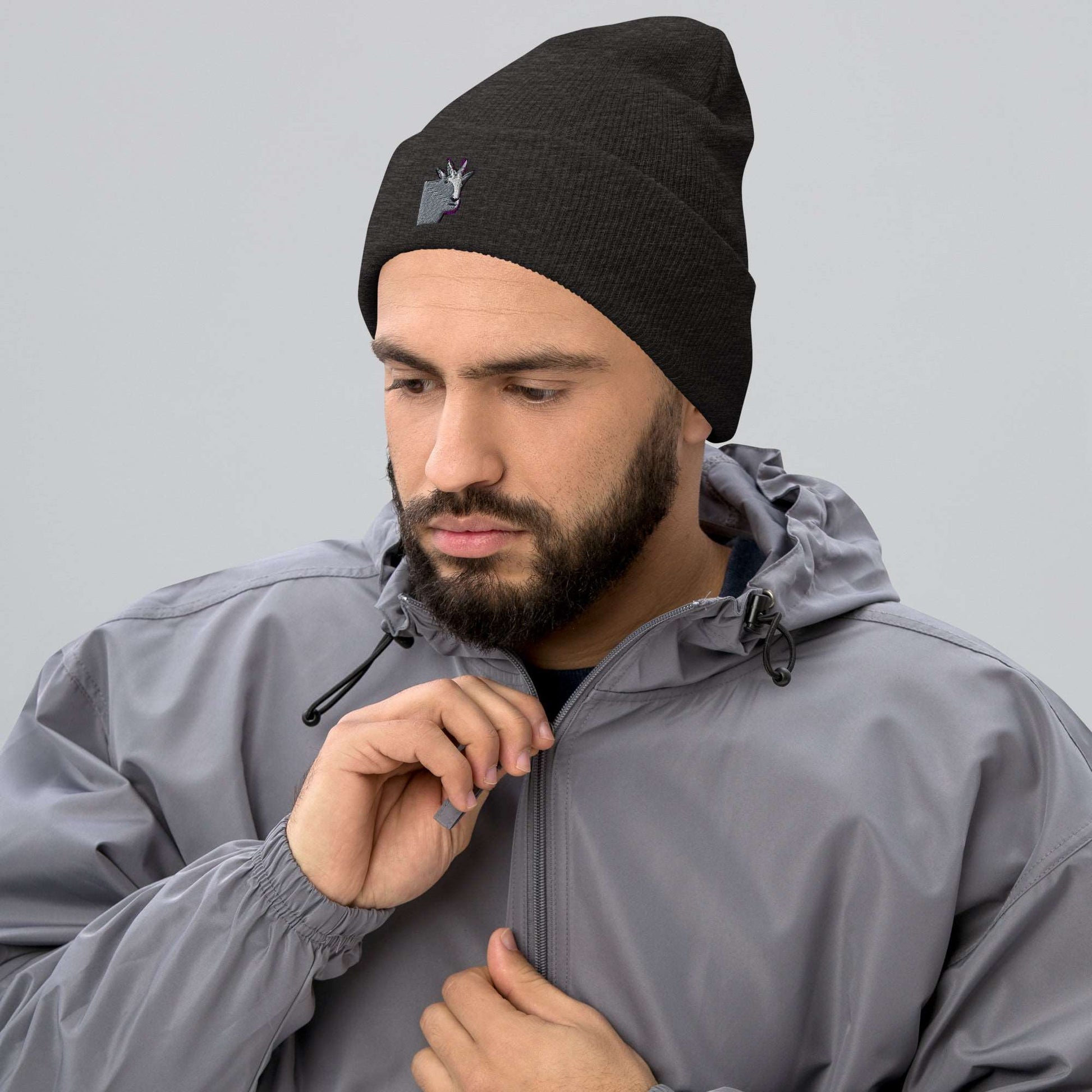 A male model wearing a high-quality dark grey unisex cuffed beanie that has an embroidery of a funny mountain goat design and a running jacket.