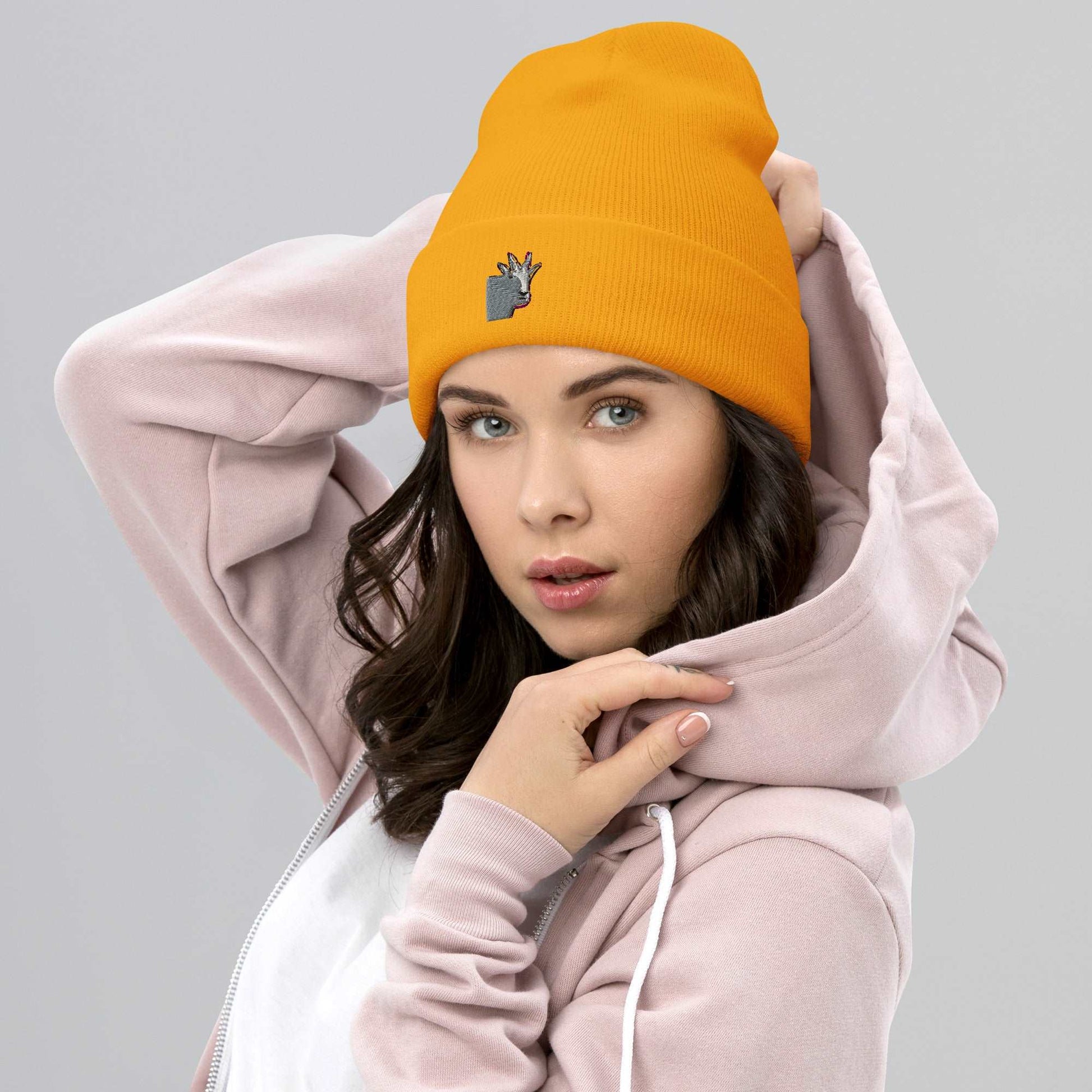 A female model wearing a high-quality yellow unisex cuffed beanie that has an embroidery of a funny mountain goat design.