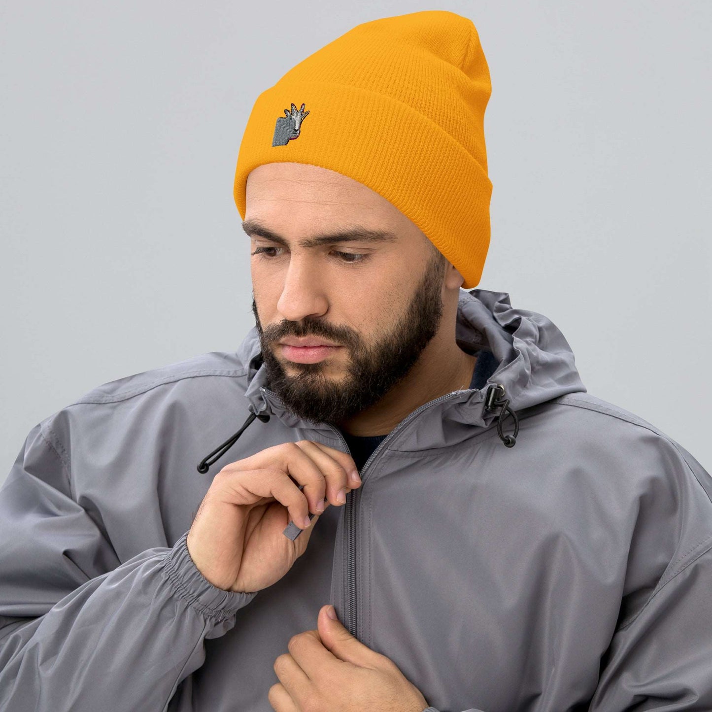 A male model wearing a high-quality yellow unisex cuffed beanie that has an embroidery of a funny mountain goat design and a running jacket.