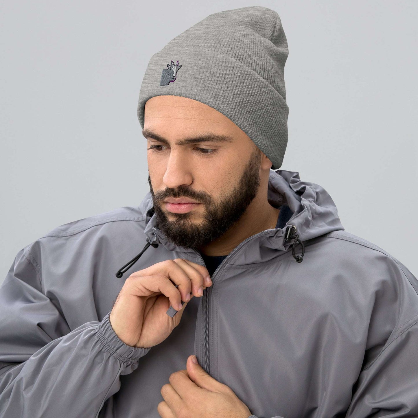 A male model wearing a high-quality light grey unisex cuffed beanie that has an embroidery of a funny mountain goat design and a running jacket.