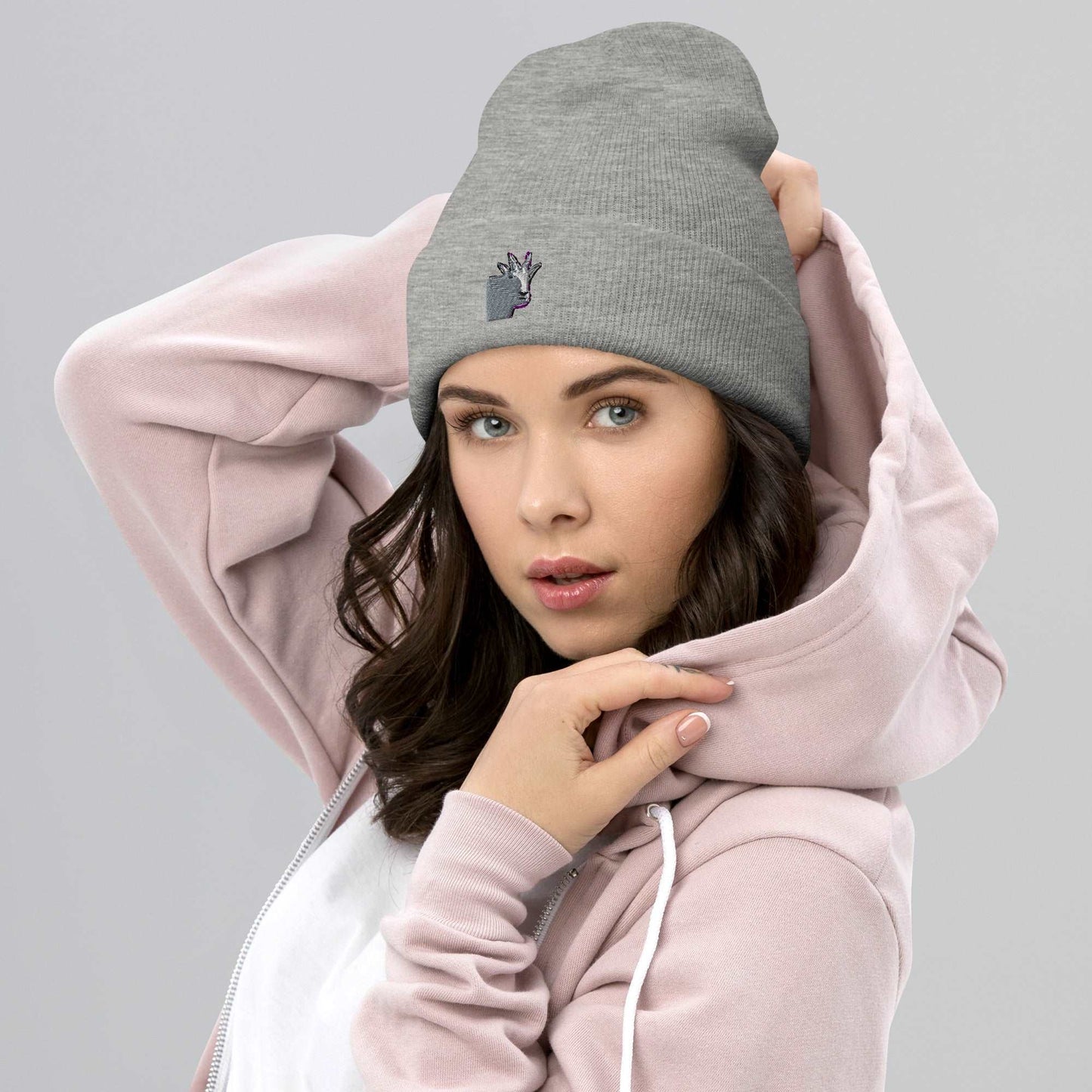 A female model wearing a high-quality light grey unisex cuffed beanie that has an embroidery of a funny mountain goat design.