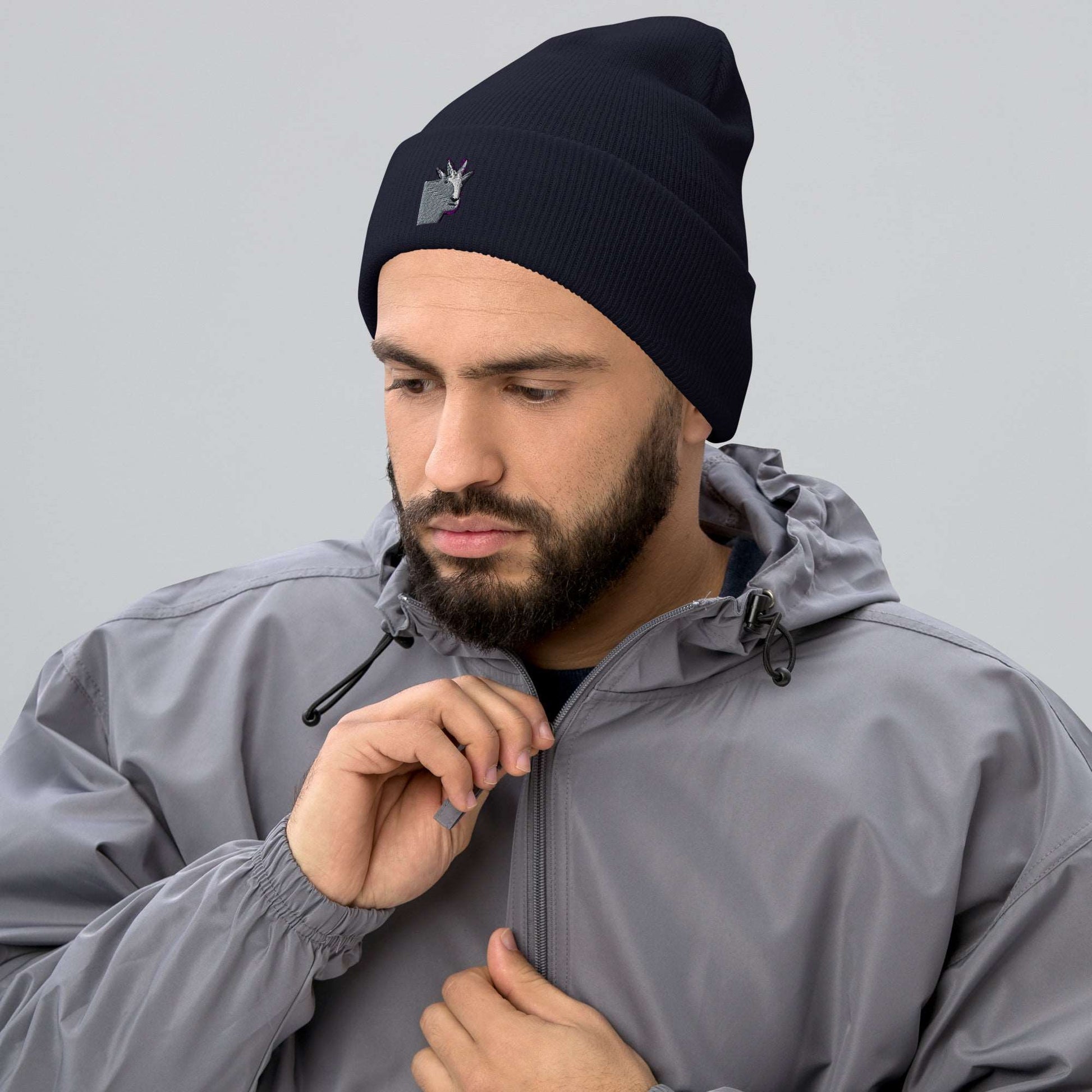 A male model wearing a high-quality navy unisex cuffed beanie that has an embroidery of a funny mountain goat design and a running jacket.