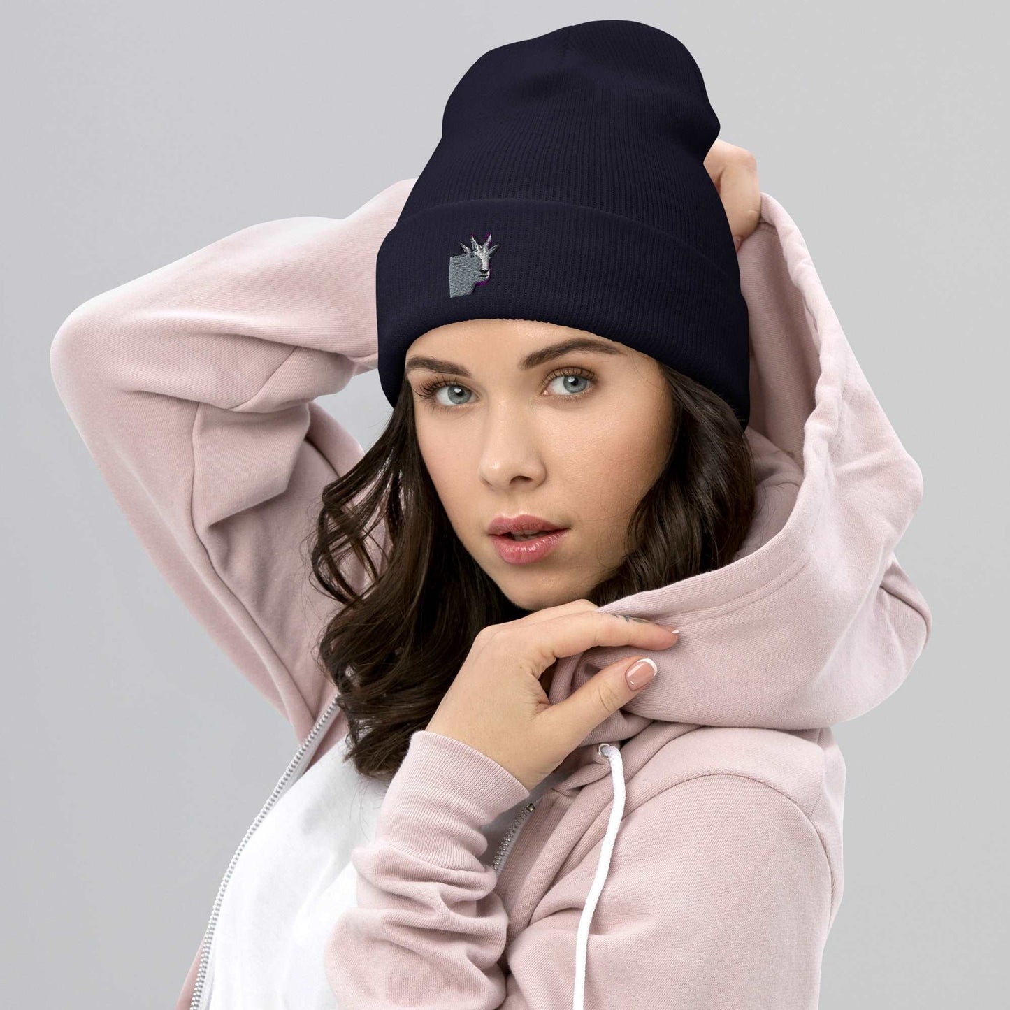 A female model wearing a high-quality navy unisex cuffed beanie that has an embroidery of a funny mountain goat design.