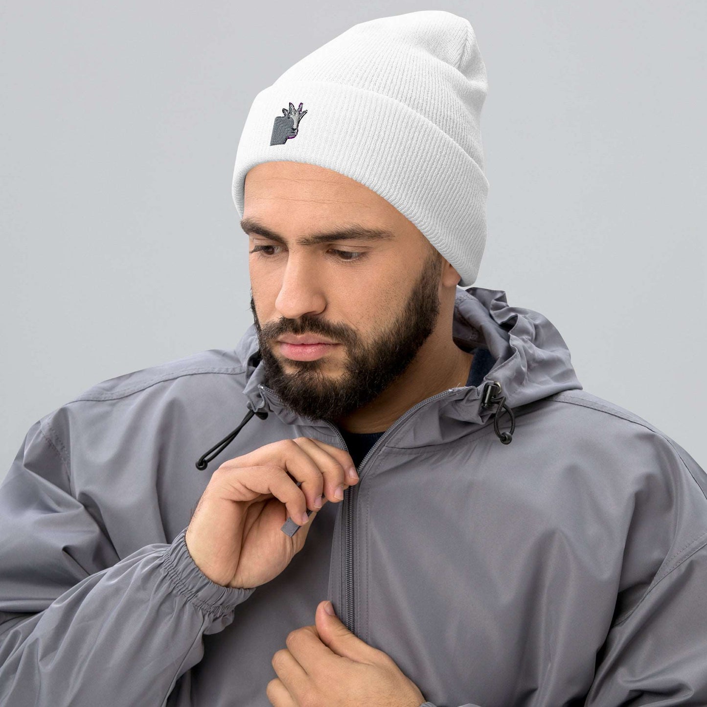 A male model wearing a high-quality white unisex cuffed beanie that has an embroidery of a funny mountain goat design and a running jacket.