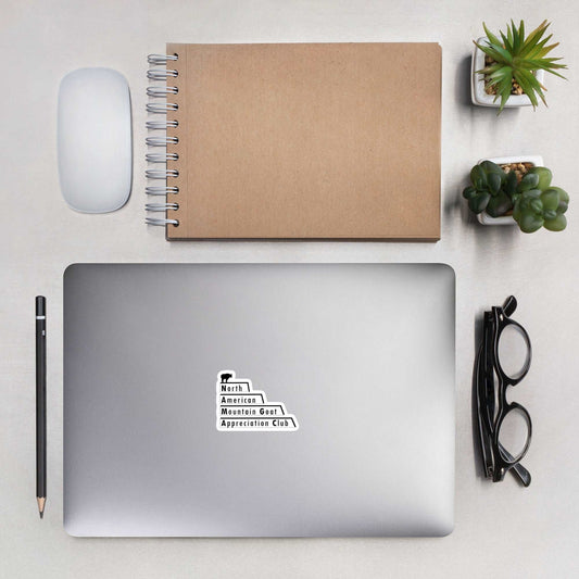 A laptop with a cover stick that is the North American Mountain Goat Appreciation Club logo, a pair of glasses, a pencil, a notebook, a mouse, and succulents