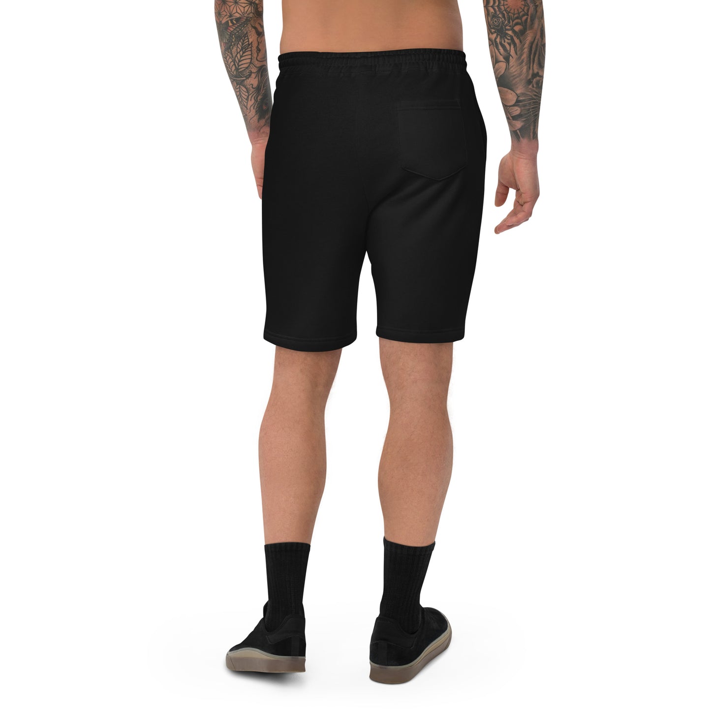 A male model with arm tattoos wearing a pair of black fleece shorts with a funny mountain goat design on the right leg and a pair of black shoes.