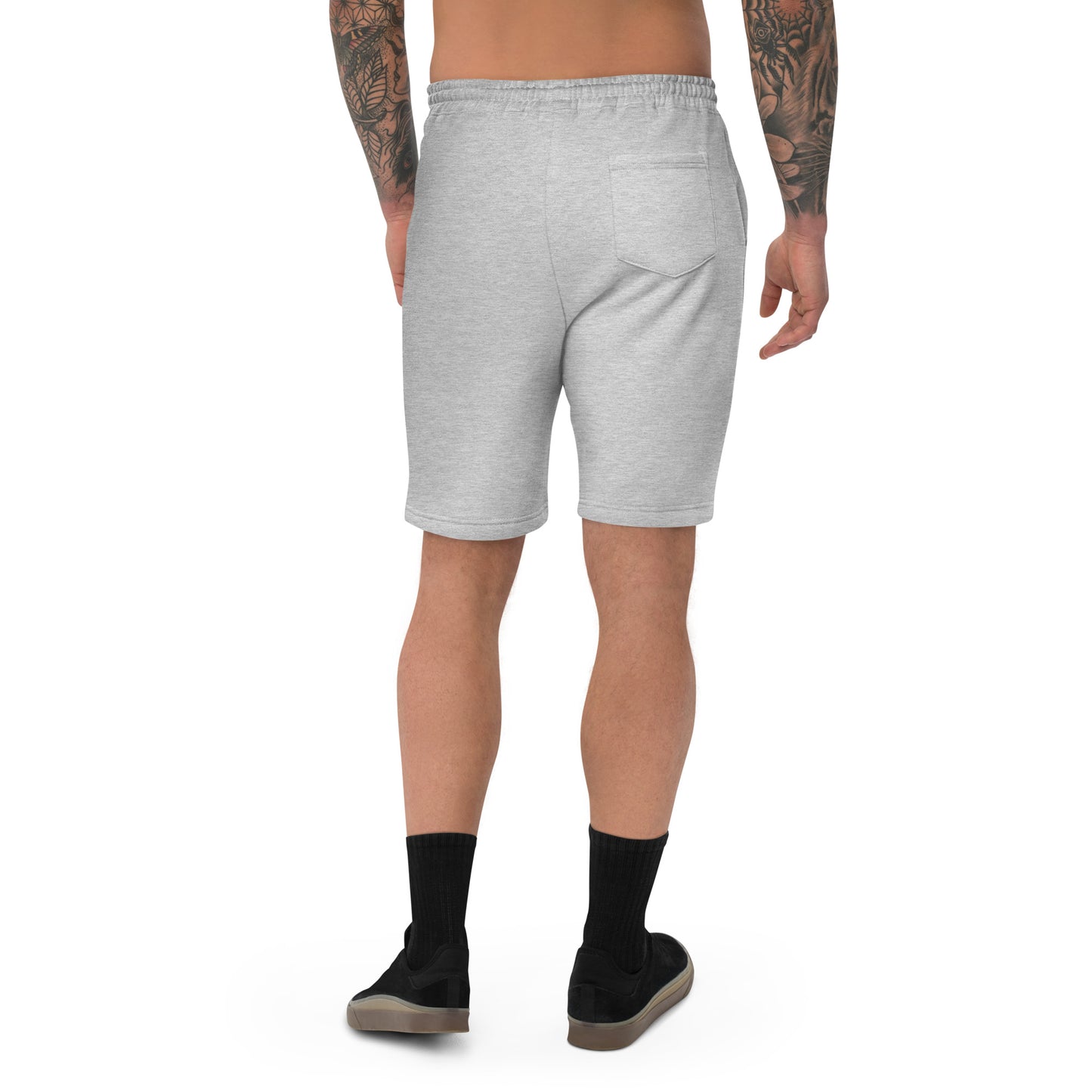 A male model with arm tattoos wearing a pair of grey fleece shorts with a funny mountain goat design on the right leg and a pair of black shoes.