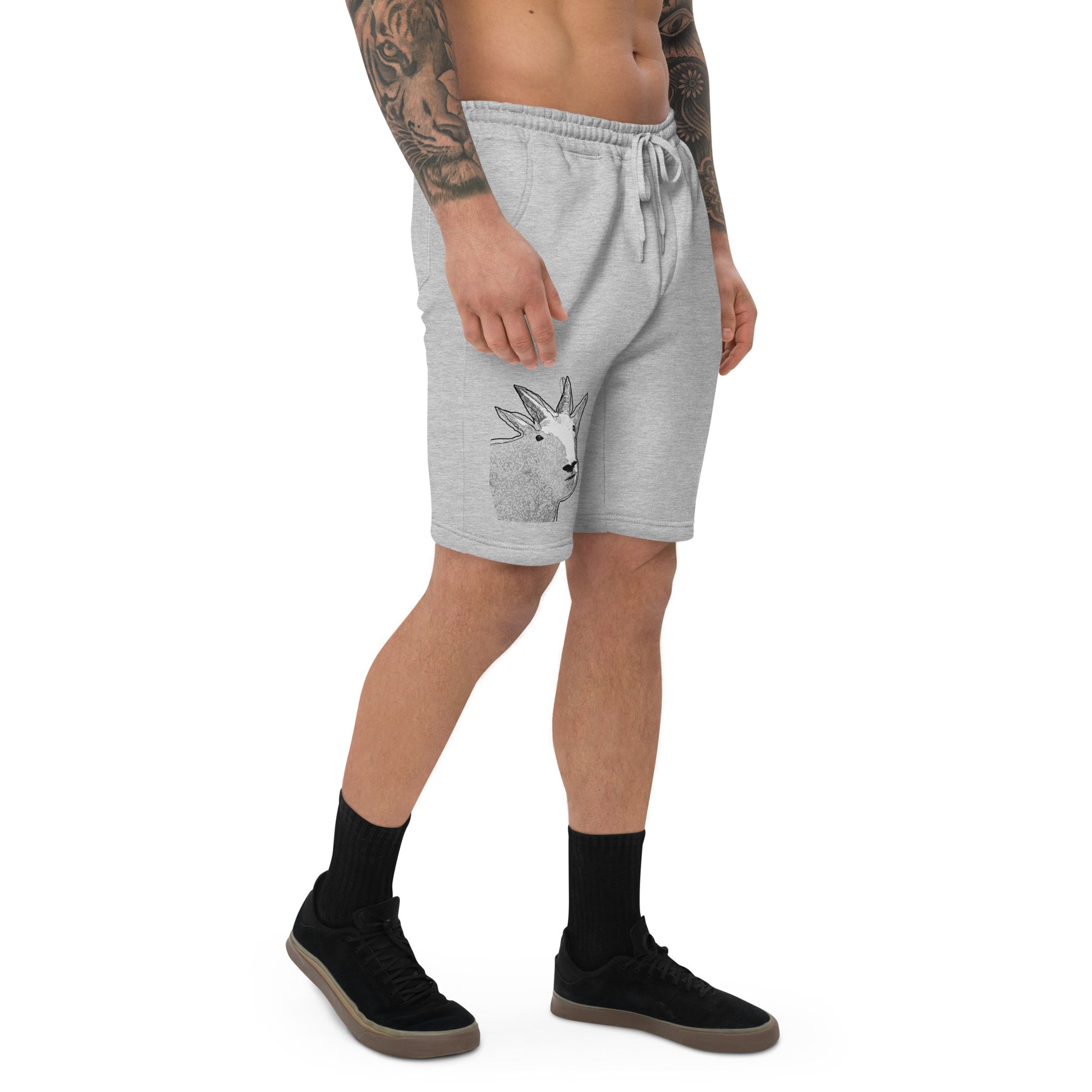 A male model with arm tattoos wearing a pair of grey fleece shorts with a funny mountain goat design on the right leg and a pair of black shoes.