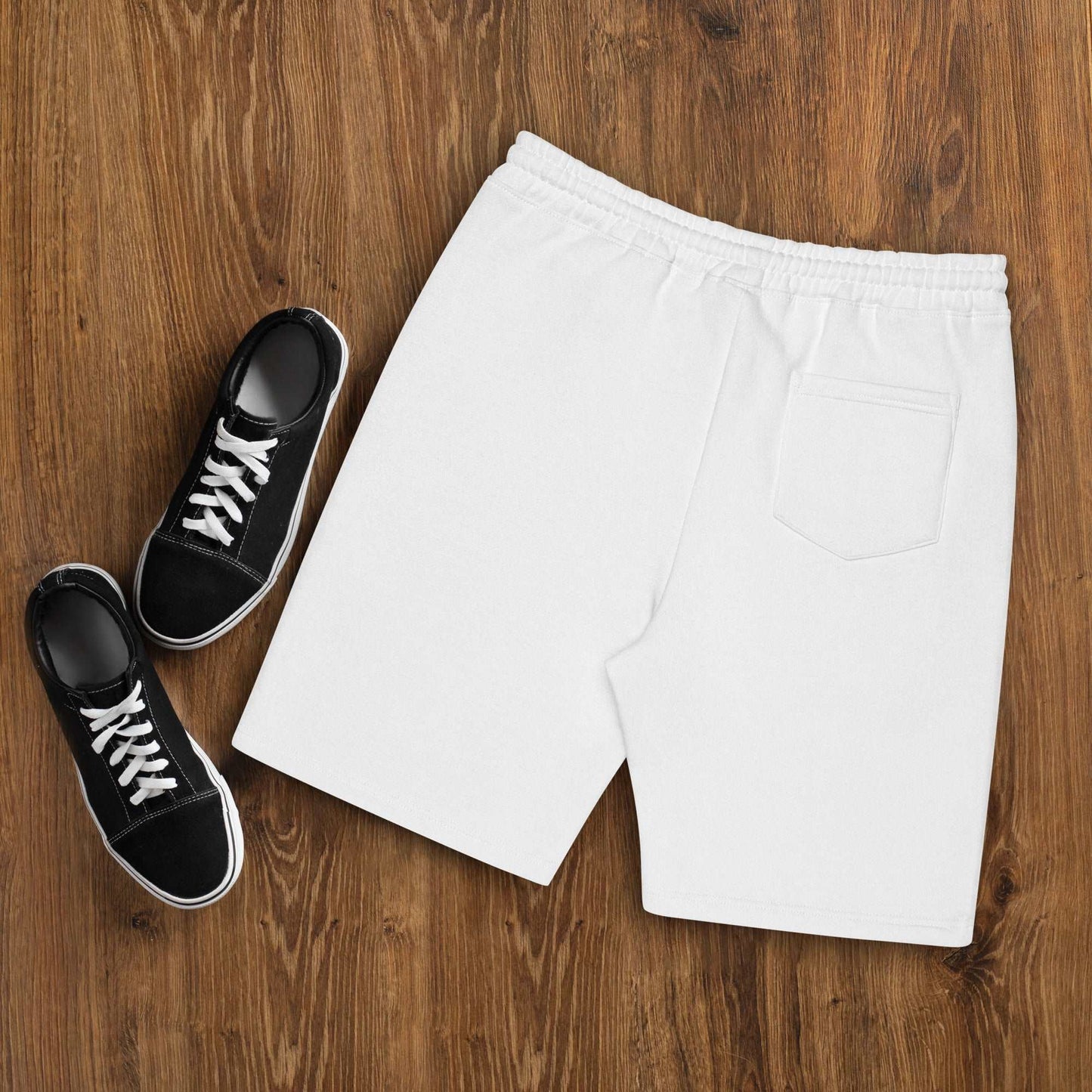 A pair of white Men's fleece shorts designed by North American Mountain Goat Appreciation Club that features a unique funny mountain goat design, placed on a natural wooden floor beside a pair of black sneakers.