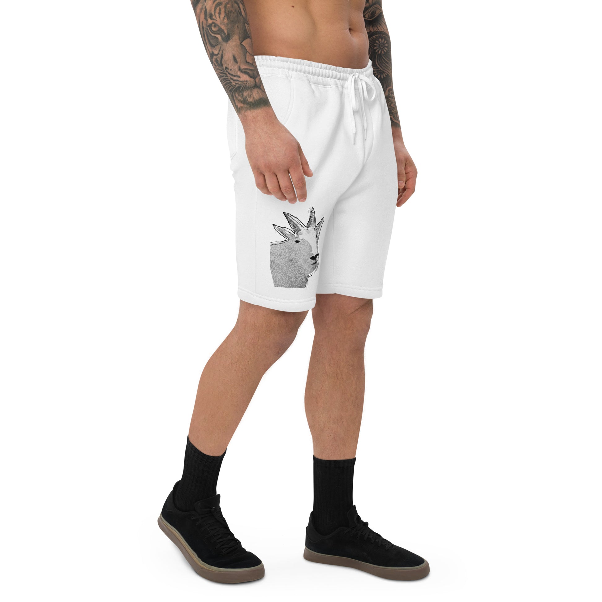 A male model with arm tattoos wearing a pair of white fleece shorts with a funny mountain goat design on the right leg and a pair of black shoes.