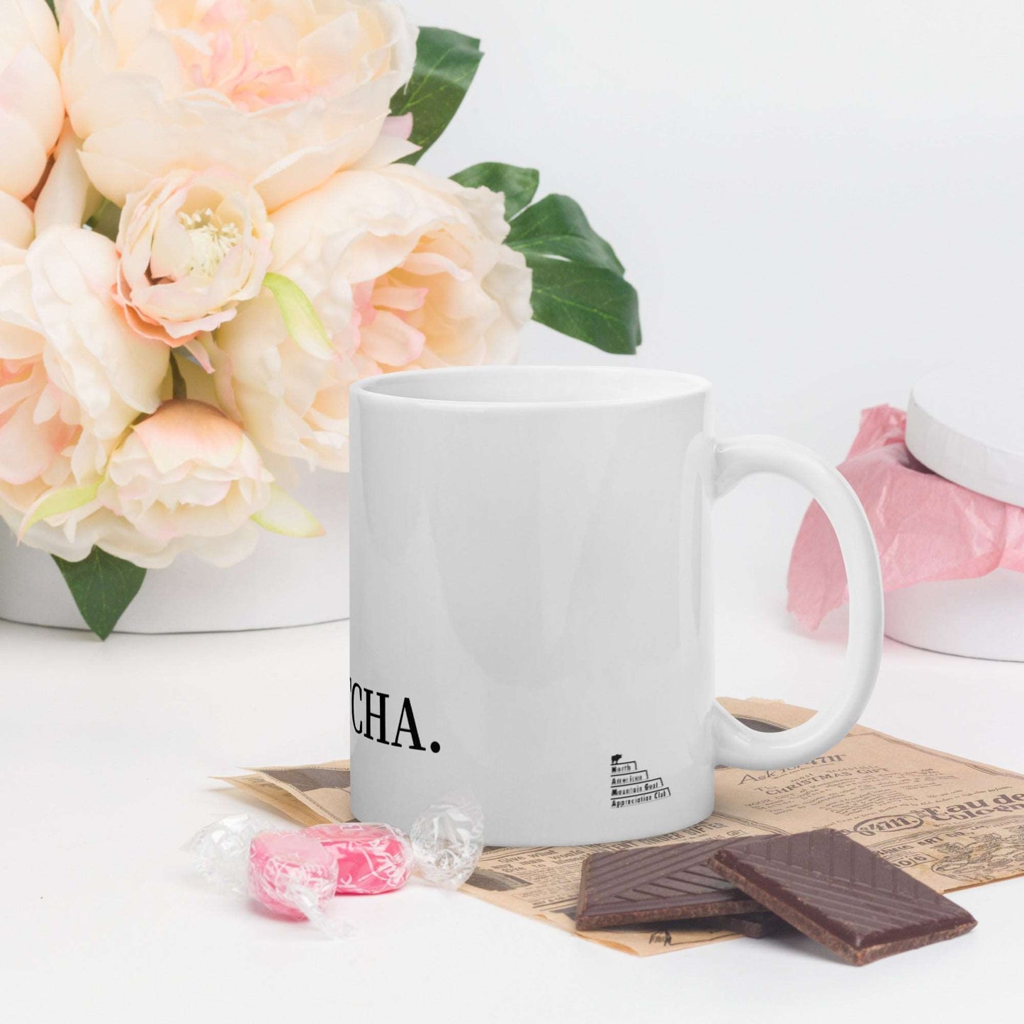 A white glossy mug that has a funny mountain goat design, the quote "GOATCHA.", and the logo North American Mountain Goat Appreciation Club.