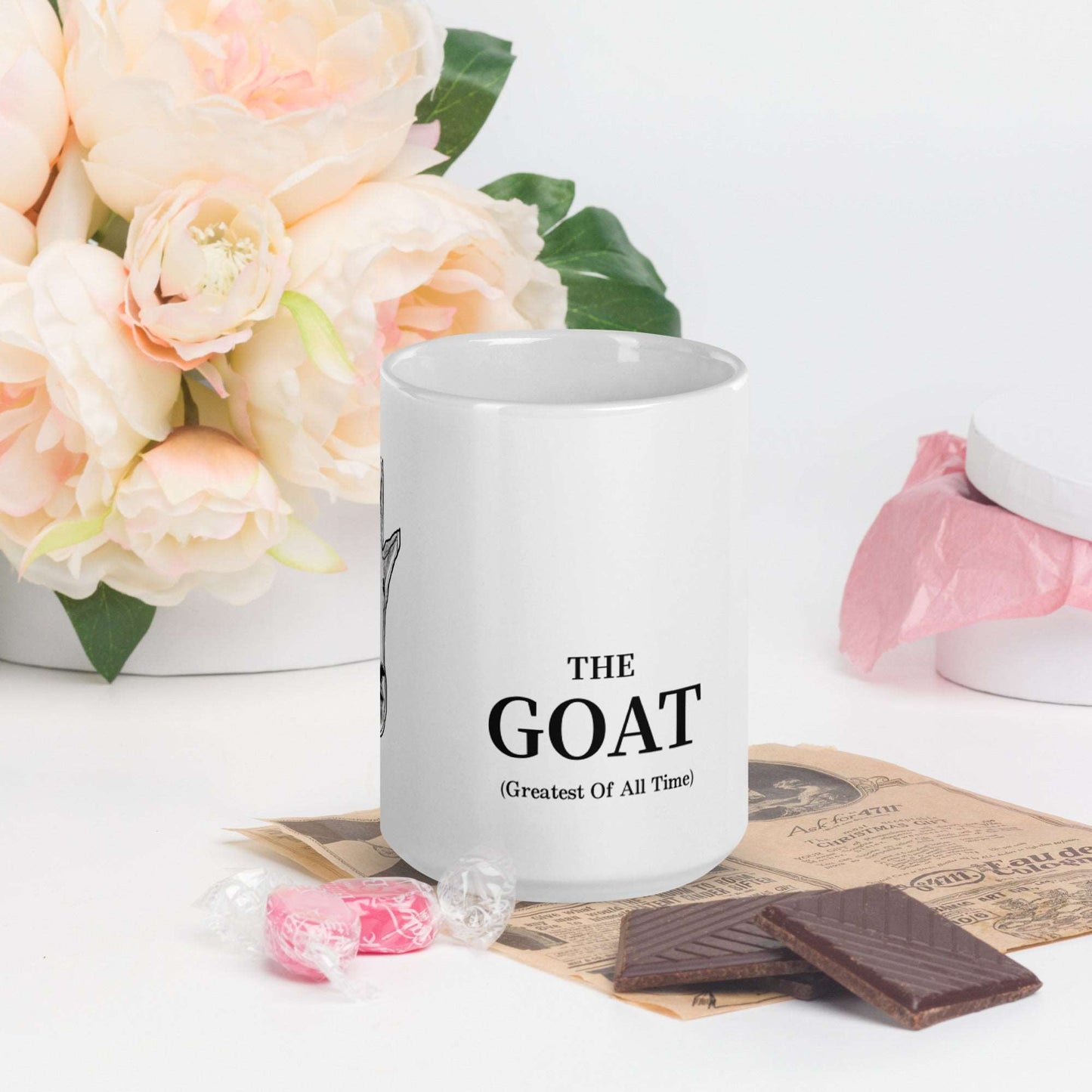 A white glossy mug that has a funny mountain goat design, the quote "The GOAT", and the logo North American Mountain Goat Appreciation Club.